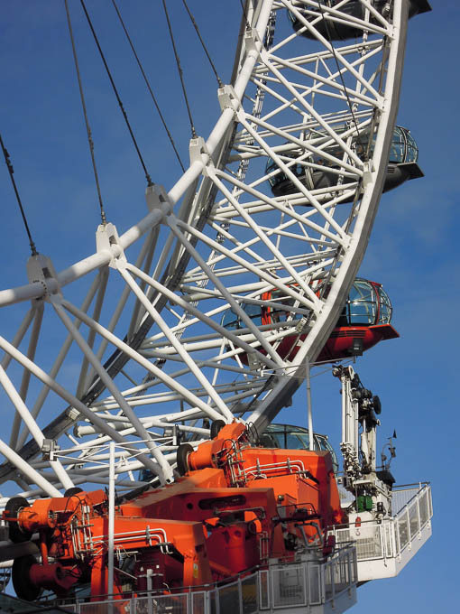Photograph, close, daytime: detail of the London Eye orange machinery including the red "key" capsule